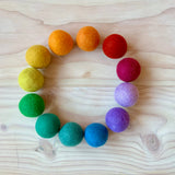 Zwölf Filzbälle für Kinder von Kokomoo in Regenbogen Farben liegen in einem Kreis.