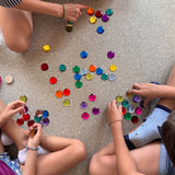 Ganz viele der zwölf Maxi Funkelsteine liegen am Boden, rundherum Kinder im Schneidersitz zum Spielen.