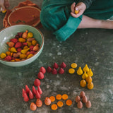 Ein Kind spielt mit dem Grapat Mandala Mix "Warm" Set bestehend aus 81 Mandalasteinen, alle in verschiedenen Formen, in Gelbtönen, Orange, Rosatönen und Rottönen.