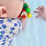 Ein Baby erkundet mit dem Mund die Babyrassel Regenbogen Karussell aus speichelecht lackiertem Holz von Nic Toys.