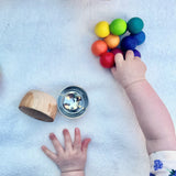 Die rechte Babyhand greift nach dem bunten Kugelgreifling aus Holz von Kokomoo, vor der linken Babyhand liegen kleine Schüsseln.