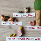 Ostheimer tierische Spielfiguren aus Holz: Katze, Maus, Hahn, Henne, Küken, Eichhörnchen, Figur Tochter. Neben dem Eichhörnchen ist ein Filzbaum mit grüner, runder Krone. Daneben liegen Namensschilder, die erklären, wer die Figuren geschenkt hat, zum Beispiel "von Onkel Paul".