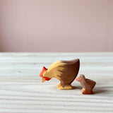 Zwei Spielfiguren aus Holz sind zu sehen: Ostheimer Huhn und ein braunes Küken. Das Huhn pickt scheinbar Futter, das Küken steht hinter der Henne.