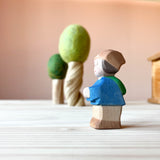 Im Vordergrund steht die Spielfigur Mo, ein kleiner Zwerg von Ostheimer und blickt seitlich nach links. Im Hintergrund stehen 2 Filzbäume.
