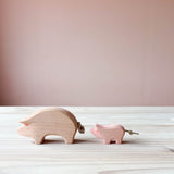 Eine Ostheimer Spielfigur aus Holz, das Schwein in rosa steht auf einer Holzplatte und schaut nach links. Dahinter steht das rosa Ferkel.