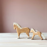 Zwei Spielfiguren aus Holz stehen hintereinander. Vorne ein Ostheimer hellbrauner Hafllinger, dahinter ein Haflingerfohlen, beide mit Blick nach links.