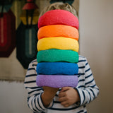 Ein Kind hält alle 6 Original Stapelstein® Mini Steine in Regenbogenfarben gestapelt vor sich.
