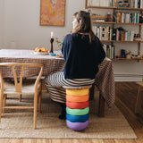 Eine Frau sitzt auf einem Hocker, der aus einem Stapelstein® Regenbogen Set Classic und einem Confetti Board zusammengebaut ist.