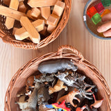 Ein runder Weidenkorb mit zwei Tragegriffen gefüllt mit Spielfiguren, daneben ein Korb mit X-Klötzen von Bauspiel und der kleine graue Jutekorb mit Lichtbauwürfel.