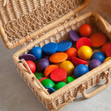 Grapat buntes Rundes "Round" mit 12 Halbkugeln, 12 Buckelplättchen und 6 Kugeln in Regenbogenfarben liegen verstreut in einem kleinen Koffer aus Weidengeflecht.