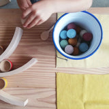 In einem kleinen Kübel aus Emaille liegen ganz viele Filzkugeln, ein Kind spielt mit verschiedenen Spielmaterialien aus Holz.