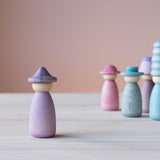 Vorne steht eine Grapat Fancy Nins Spielfigur in lila mit einem gleichfarbigem Hut, im Hintergrund weitere Spielfiguren aus Holz in Blau, Lila und Rosa.