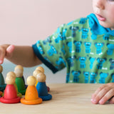 Ein Kind berührt konzentriert einen der bunten Holzfiguren von Grapat. Es stehen 8 bunte Nins vor ihm, jeweils in einem Holzring in der passenden Farbe.