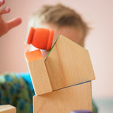 Gestapelte Holzbausteine Grapat "Houses" mit bemalten Dächern in Regenbogenfarben, ganz oben ein oranges Grapat "Mates" Holztöpfchen.