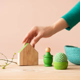 Ein Grapat Haus, ein Mates Holztöpfchen mit einer Nin Spielfigur darin, ein Grapat Bowl mit einem Kokomoo Häkelball, ein Jutekörbchen, alles in grün.