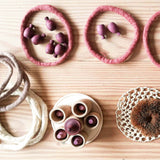 Grapat Mandala Legematerial "Pineapple" in Lilatönen liegen in farblich passenden Filzringen, daneben weiteres Filzringe in beige und weiß, Holztöpfchen und anderes offenes Spielmaterial.