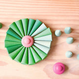 Grapat "Green Cone" - grüne Mandala Steine in Kegelform und ein rosa Mandalastein in Bütenform sind zu einer großen, runden Blüte aufgelegt.