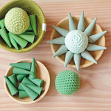 Grapat "Green Cone", Mandale Steine in Kegelform und drei Häkelbälle von Kokomoo liegen in Holztellern und einem Jutekorb, teilweise chaotisch, teilweise zu einer Sonne gelegt.