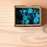 Die Mandala Steine Grapat "Little Coin" in Plättchen-Form in verschiedenen Blau-Tönen liegen in ihrer Verpackung.