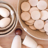Freies Spiel mit Spielmaterial aus Holz: Grapat Coins Plättchen in einem Jutekorb, Holzeier in einem anderen, Spielfiguren aus Holz.