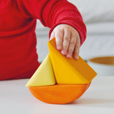 Eine Kinderhand hält das gelbe kleine Schiff aus Holzbausteinen, eins von vier Schiffen im Grimms Schaukelschiffe Steckspiel Set für Babys ab 1 Jahr.