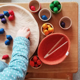 Ein Kind sortiert die bunten kleinen Holzeicheln in Regenbogenfarben vom Sortierspiel Grapat "Acorns & Bowls".