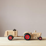 Der Fagus Traktor aus Holz von der Seite, ein kleiner Anhänger aus Holz mit einem Zapfen als Ladung ist angekoppelt.