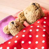 Zwei Kuschelbären schlafen zugedeckt unter dem roten Tupfentuch von Kokomoo, nur ihre Köpfe sind zu sehen.