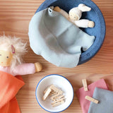 Ein weißer Wichtel von Nanchen liegt in einem blauen Stapelstein®, zugedeckt mit einem hellblauen Stricktuch, daneben eine Emailleschüssel mit kleinen Wäscheklammern aus Holz.