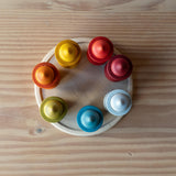 Die sieben Nins Holzfiguren vom Set Grapat 7 Moons stehen im Kreis in ihren sieben Holzbechern, auf einem flacher Holzteller.