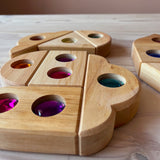 "Funkeldächer" Holzbausteine mit bunten Funkelsteinen aus Acryl von Bauspiel in verschiedenen Formen sind auf dem Boden zu einem Muster gelegt.