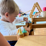 Ein Kind steckt sehr konzentriert kleine, bemalte Holzteile aus dem Set Fancy Nins von Grapat in Löcher eines Holzregals.