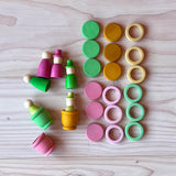 Grapat Holzfiguren-Set "Aquamarina Spring" alle 45 Teile aufgelegt: 3 Töpfchen, 6 Nins, 9 Holzplättchen und 9 Holzringe in den Farben rosa, grün und gelb.
