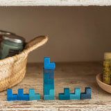 Die eckigen, Tetris-artigen Grapat Mis, Match and Bloom Holzsteine in verschiedenen Blautönen sind teilweise übereinander, teilweise nebeneinander aufgebaut. Links steht ein Korb, rechts eine Holzschale.
