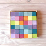 Die 36 Holzbausteine in Würfel Form von Grimms Regenbogen Pastell Mosaik liegen  im quadratischen Holzrahmen.