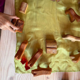 Die Holzbausteine Wald und Spielfiguren aus Holz stehen auf einem grünen Spieltuch aus Seide, das wohl eine Wiese ist im freien Spiel.