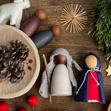 Zwei kleine Holzfiguren von Grapat, mit Stoffen zu Maria und Josef verkleidet, darüber ein Weihnachtsstern aus Stroh. So werden Spielfiguren zu Krippenfiguren für die Weihnachtskrippe.