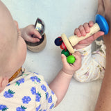 Zwei Babys spielen mit der Regenbogenrassel von Nic Toys. Ein Baby hat noch kleine Klangschalen in der anderen Hand.