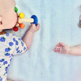 Ein Baby auf dem Bauch liegend erkundet mit dem Mund den Baby Greifling Rassel Karussell von Nic aus speichelecht lackiertem Holz.