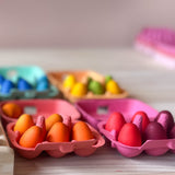 Zwei kleine Eierkartons in pink und orange gefüllt mit kleinen Holzeiern in der passenden Farbe.
