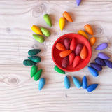 Grapat "Rainbow Snowflakes" Mandalasteine in Schneeflocken-Form liegen am Boden verstreut, bis auf alle roten Teile, die liegen in einer roten Holzschale.