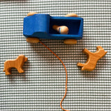 Babygreifling Hund und Pferd von Ostheimer liegen auf einem karierten Tuch, dazwischen der blaue Nachziehlastwagen aus Holz mit einer Spielfirgur darin.