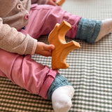 Ein sitzendes Baby hält das Holzpferd von Ostheimer in einer Hand, ein perfekter Greifling.