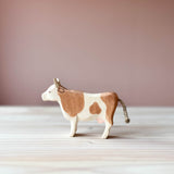 Ostheimer Kuh Spielfigur für Kinder aus Holz mit braunen Flecken, steht mit erhobenem Kopf und Blick nach links.