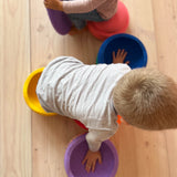 Zwei Kinder krabbeln über am Boden aufgelegte Stapelsteine in Regenbogefarben.