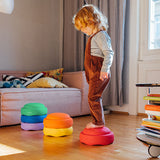 Ein Stapelstein® Bundle Classic in Regenbogenfarben in drei verschiedenen Teilen, mal drei, mal zwei gestapelt, mal ein loser Stein. Ein Kind balanciert darüber.