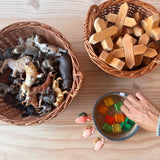 Ein großer runder Weidenkorb von Kokomoo gefüllt mit Spieltieren, daneben der kleinere, runde Weidenkorb mit X-Klötzen und das kleine Jutekörbchen mit Lichtbauwürfel.
