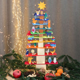 Grimms Regenbogen Bauplatten in rechteckiger Form sind mit anderen Bausteinen und Holzwürfeln sowie kleinen Spielfiguren aus Holz zu einem Weihnachtsbaum aufgebaut. Rundherum Dekoration mit Granatäpfel, Orangen, Nüssen und Tannenzapfen.