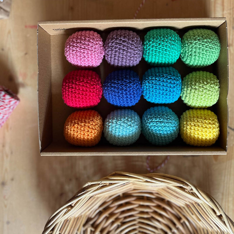 12 Häkelbälle von Kokomoo in Regenbogenfarben sortiert in einer Kartonbox.