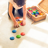 Ein Kind spielt mit dem offenen Spielmaterial Grapat buntes Rundes "Round" am Boden, neben ihm ein kleiner Koffer aus Weidengeflecht mit den Holzspielsachen.